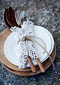 Cutlery tied up in lace doily on stack of plates and wooden boards