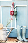 Small hanging baskets hand-crocheted from jute yarn hanging on blue and white country-house door above zinc watering can and wellington boots