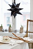 Advent crafting with white paper stars and cinnamon sticks on table; black, star-shaped lampshade in background
