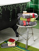 Metallhocker im Vintagelook mit Handtuchstapel; daneben eine freistehende, grüne Badewanne mit aufgemaltem Seifenblasenmuster