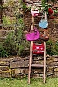 Various hand-made felt bags hanging from ladder against stone wall