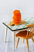 Small stack of sliced raw carrots on miniature chopping board with dolls' house furniture