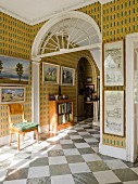 Entrance hall of English country manor house with diagonal, chequered marble floor tiles and gallery of pictures on patterned wallpaper
