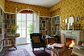 Bookcases built into niches and lounge chair in front of open fire in study of English country manor house