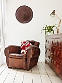 Vintage leather armchair next to antique chest of drawers on white wooden floor