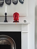 Red, ceramic head of Buddha next to black candlestick on mantelpiece