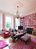 Grand interior in hot pink with pink animal-skin rug and large gallery of pictures on chimney breast above open fireplace; silver beanbag under coffee table