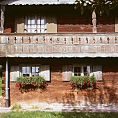 Natural patina of weathered facade with balcony and window boxes of trailing geraniums