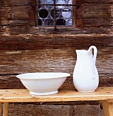 Handgetöpferte Waschschüssel und Krug auf Holzbank vor historischer Holzfassade