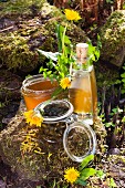 Various dandelion products; jelly, liqueur, pickled buds and freshly picked dandelions on stone outdoors