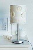 Table lamp lampshade decorated with flower-shaped sections of crocheted doily and gossamer-thin lace trim