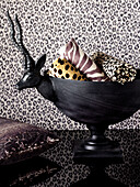 Rolls of fabric in animal-skin prints in bowl with antelope head