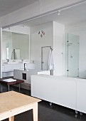 Weisses Sideboard auf Rollen neben offenem Waschbereich in loftartigem Raum