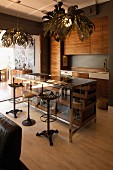 Vintage barstools at counter with glass-fronted drawers in open-plan, fitted kitchen with pendant lamps with lampshades made from stylised leaves