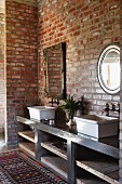 Washbasins on washstand with shelving against brick wall below vintage mirror with metal frame