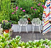 White, perforated shell chairs on terrace in front of flower bed; striped parasol in foreground