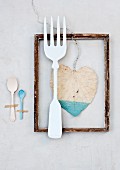 Still-life arrangement of vintage fork on wooden picture frame with painted leaf and spoons stuck down with tape