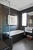 Dark, plain walls in bathtub area and mosaic tiles above sink and in shower cabinet behind glass door