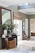 Antique console table and mirror against wall painted olive green and animal-skin rugs on floor
