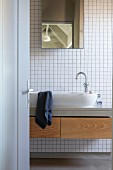 Blick durch geöffnete Badezimmertür auf Waschtisch mit ovalem Waschbecken und Schubladen mit Holzfronten; Spiegelschrank auf Rückwand mit weissen Mosaikfliesen