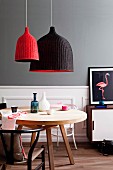 Retro-style living area with red and black, wicker pendant lamps above round, wooden table in front of grey wall with white wood-panelled dado