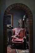 View through brick archway into dark corner with old, leather lounge chair in spotlight