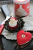 Christmas table decoration with Father Christmas candle in small cake tins, cutlery and fabric heart