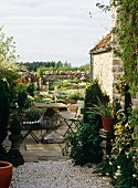 Blick auf üppig bepflanzte, gepflasterte Terrasse mit Steintisch & Klappstühlen