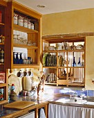 Küche im Landhausstil mit gelben Wänden, blau gefliesten Arbeitsflächen & Holzregalen für Geschirr