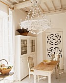 Esszimmer in Weiß mit Holztisch & Stühlen, Vitrinenschrank, Kronleuchter & ornamental verzierter Tür
