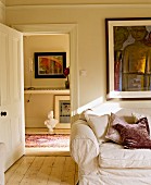 Wohnzimmer mit Dielenboden, Sofa & Wandbild sowie geöffneter Tür zum Flur