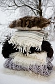 Stacked woollen blankets, furs and fur-covered cushion in snow