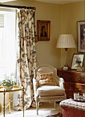 Wohnzimmerecke im altenglischen Landhausstil mit Polstersessel vor floral gemustertem Vorhang und zierlichem Beistelltisch