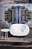 White chair and side table in front of house wall painted with graffito