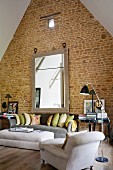 Oversized mirror on tall gable wall of converted barn in living area with comfortable grey and white sofa set and reading lamp