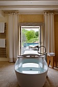 Freistehende Badewanne mit Holzablage; im Hintergrund offene Terrassentür mit Blick auf den Pool