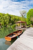Rowing boat next to wooden jetty with summer house; wooded hills in background