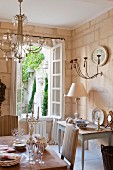 Esszimmer mit Shabby-Chic Flair in nostalgisch romantischem französischen Landhaus, Blick durch geöffnete Sprossenfenster in begrünten Innenhof