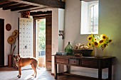 Hund im Eingangsbereich eines Landhauses, Sonnenblumen in Vase auf rustikalen Holz Wandtisch