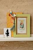 Vintage ornaments on bookshelf - paper butterfly on decorative book, Tibetan prayer tassels on framed picture of the Madonna and old enamel sign with the number 4