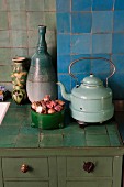 Old kettle, vases & bowl of onions on tiled kitchen worksurface