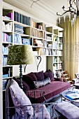 Wohnraum mit lila Couch & lila Sitzmöbeln vor Bücherwand