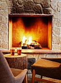 Warm drinks on tree stump used as side table and upholstered chairs in front of open fireplace