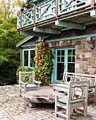 Outdoor Sitzgarnitur um Steinbrocken auf Terrasse vor Natursteinhaus mit Balkon und hellgrün lackiertem Holzgeländer