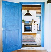 Blick durch eine blaue Holztür auf modernen Küchenherd in rustikaler Küche