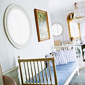 Zierliches, antikes Tagesbett vor holzvertäfelter Wand mit Bullaugenfenster