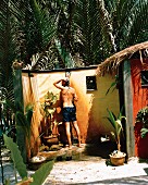 Mann in gemauerter Dusche unter freiem Himmel, umgeben von tropischen Pflanzen