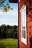 Rotbraunes Holzhaus mit weißem Fenster und Blick auf Landschaft mit Wald