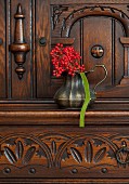 Rote Beeren in Vase aus Metall auf geschnitzter Kommode