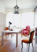 White table and antique chairs in grand interior with wrapped chair in bay window